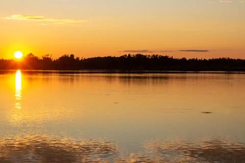A colorful sunny sunset is reflected on the surface of the calm lake. Stock Photos