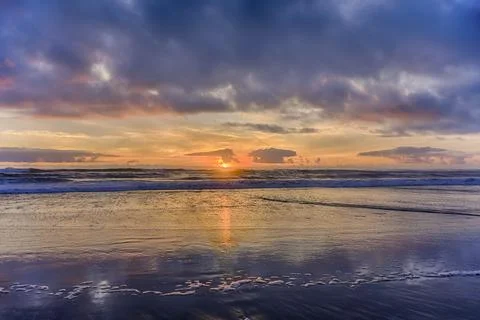 Colorful sunset over the ocean with waves and reflective wet sand at a coas.. Stock Photos