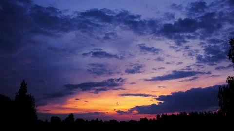 Colorful sunset sky with dark cloud silhouettes and a gradient from deep blue Stock Footage 343781556