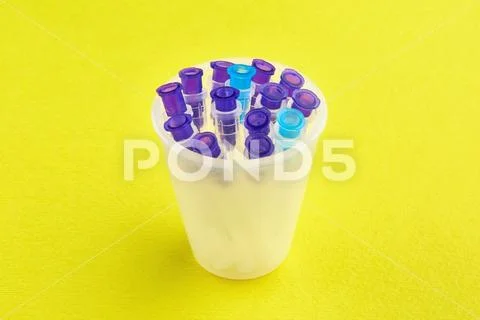 Colorful syringe needles in measuring glass on yellow background Stock Photos