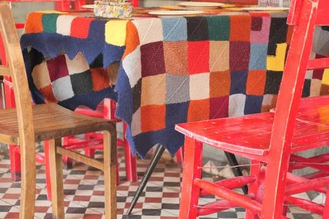 Colorful table with patchwork cover and red chairs in cozy cafe 库存照片