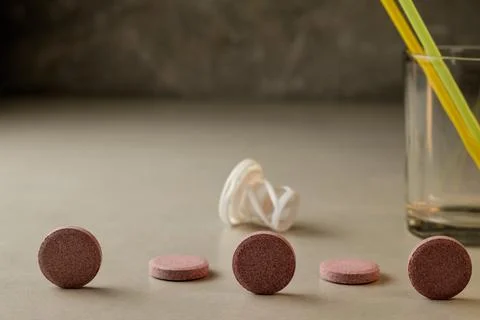 Colorful tablets lined up on a surface next to a glass and straws Stock Photos