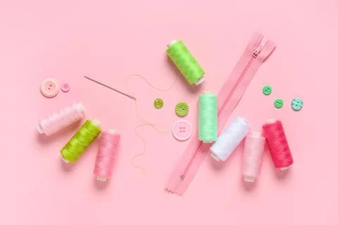 Colorful thread spools with buttons, zipper and needle on pink background Stock Photos