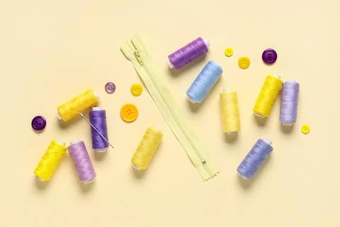 Colorful thread spools with buttons, zipper and needle on beige background Stock Photos