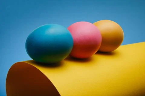 Colorful three Easter eggs on a rolled sheet of paper against a blue backgrou 스톡 사진