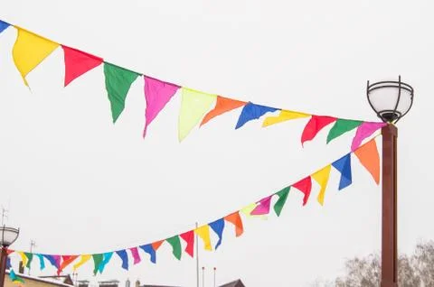 Colorful triangular cloth flags hanging on ropes tied to a lamppost, decorati Stock Photos