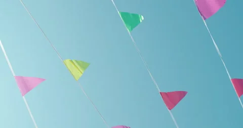 Colorful triangular flags flutter on strings against a clear blue sky, evoking a Stock Footage 311236370