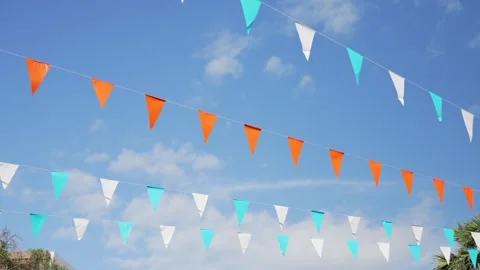 Colorful triangular flags hanging outdoors against blue sky, creating a cheerful Stock Footage 323785453