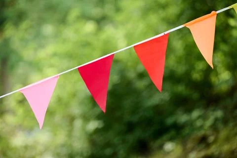 Colorful triangular pennant flags hanging outdoors with lush green background Stock Photos