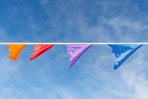 Colorful triangular pennant flags hanging on a line against bright blue sky Stock Photos