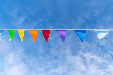 Colorful triangular pennant flags hanging on a line against bright blue sky Stock Photos