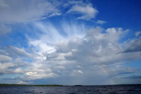 Colorfull rainbow under single cloud over lake Stock Photos