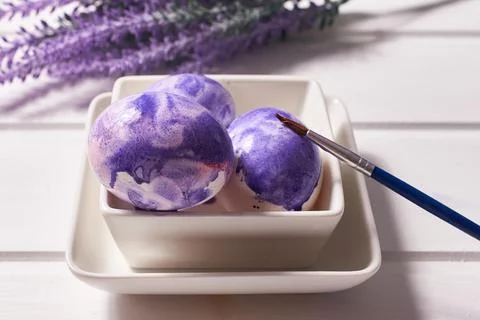 Coloring eggs with a brush. Easter tradition. Painted eggs on a white wooden Stock Photos