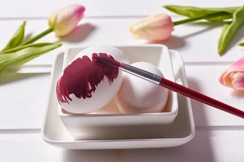 Coloring eggs with a brush. Easter tradition. Painted eggs on a white wooden Stock Photos