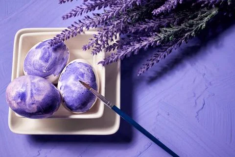 Coloring eggs with a brush. Easter tradition. Painted eggs on a purple waterc Stock Photos