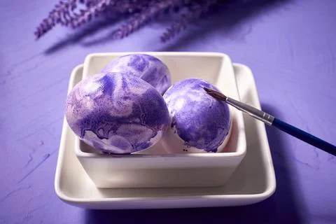 Coloring eggs with a brush. Easter tradition. Painted eggs on a purple waterc Stock Photos