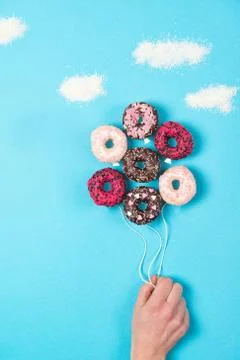 Coloured mini donuts on blue background, creative food idea, hand holding donuts Stock Photos