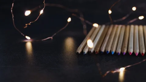 Coloured pencils lined up on dark desk with  fairy lights and camera panning  Stock Footage 116645660