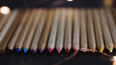 Coloured pencils lined up on dark desk surrounded by fairy lights with camera Stock Footage 116645773