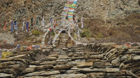 Coloured prayer flags flapping above stone stairs to Milarepa cave, Nepal Stock Footage 124677372