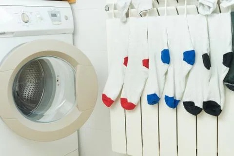 Coloured socks drying on the heating radiator next to the washing machine. Stock Photos