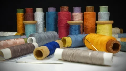 Coloured spools of thread lie on white table on black background, tilt view Stock Footage 315439397