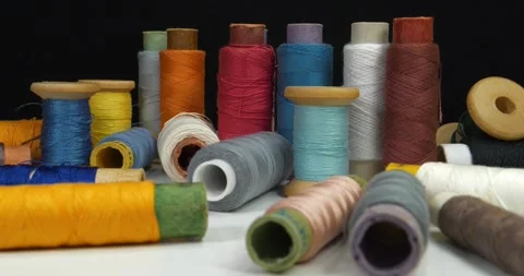 Coloured spools of thread lie on white table on black background, zoom-in video Stock Footage 317048753