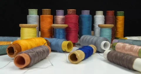 Coloured spools of thread lie on white table and rotates on black background Stock Footage 318035340