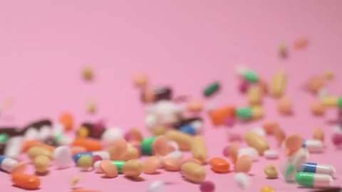 Coloured tablets and pills falling down on pink background Video stock 168173074