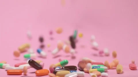Coloured tablets and pills falling down on pink background Video stock 168173131