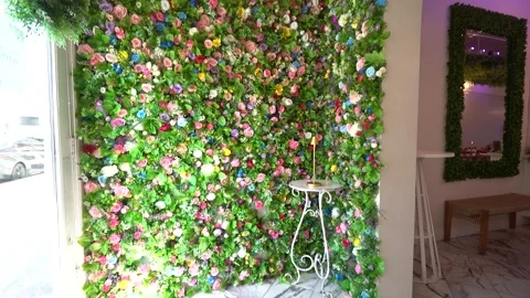 Colourful artificial flower wall with a small table and lamp Stock Footage 345549909