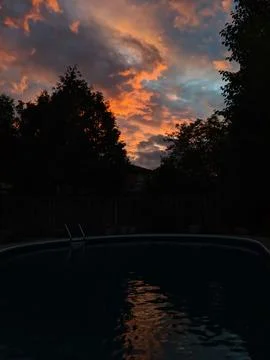 Colourful clouds at sunset reflect off a dark swimming pool Foto stock