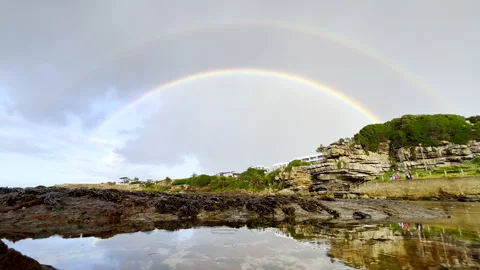 Colourful double rainbow in sky over calm water in tidal pool, Hermanus. Stock Footage 336729329
