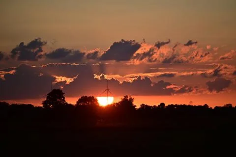 Colourful dramatic sky with clouds and a wind turbine during sunset Stock Photos