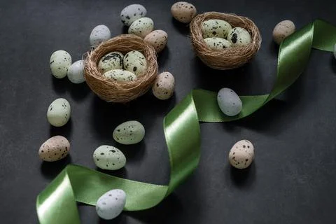 Colourful Easter eggs with bird's nest and green satin ribbon on dark bakcground Stock Photos