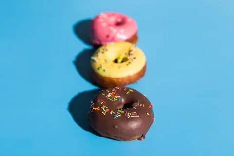 Colourful round donuts at bright blue background. Sweet donuts. Trendy sunlight Stock Photos
