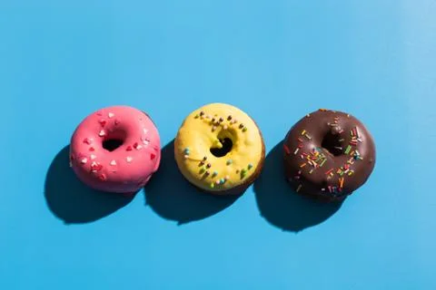 Colourful round donuts at bright blue background. Sweet donuts. Trendy sunlight Stock Photos