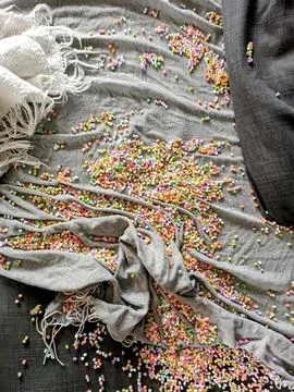 Colourful small tiny beads are laying in a mess on a sofa covered with blankets 스톡 사진