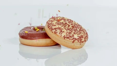 Colourful sprinkles are falling down on two doughnuts Stock Footage