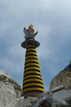 The column of a stupa, with black and yellow stripes, rises above some rocks. Stock Photos