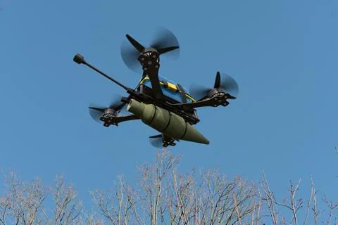 A combat drone flies over the trees, carrying suspended ammunition on a sling Fotos de archivo