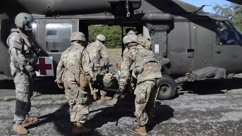 Combat Medics loading casualty lying on stretcher onto Black Hawk helicopter Stock Footage 84635486
