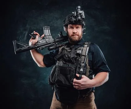 Combative man poses in dark background with rifle looking at camera Fotos de archivo