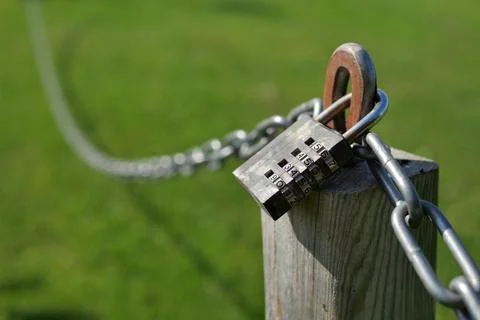 Combination lock secures a chain attached to a wooden post Stock Photos