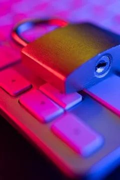A combination lock sits on a computer keyboard illuminated in colorful lighti Stock Photos