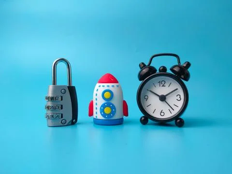 A combination padlock, a toy rocket, and a small black alarm clock stand ar.. Stock Photos