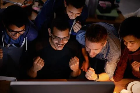 Come on a get there. a group of young man cheering at a monitor in a dark room. Stock Photos