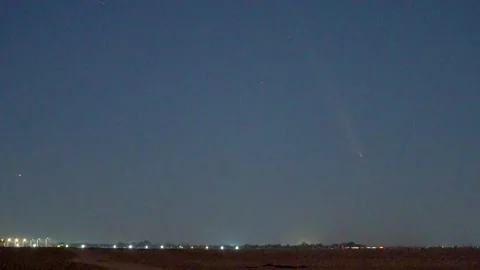 Comet ATLAS shining in the night sky over a horizon with distant lights. Видео 345046744
