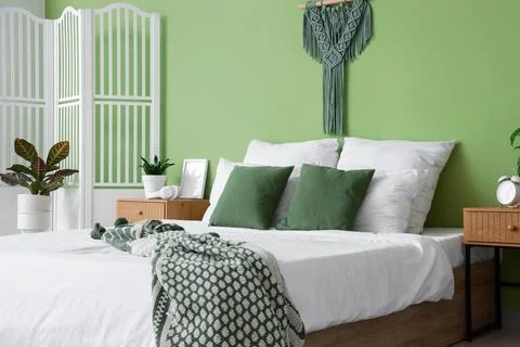 Comfortable bed, bedside table and folding screen in interior of bedroom Stock Photos
