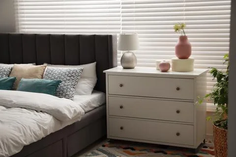 Comfortable bed with cushions and different decor elements on chest of draw.. Foto stock
